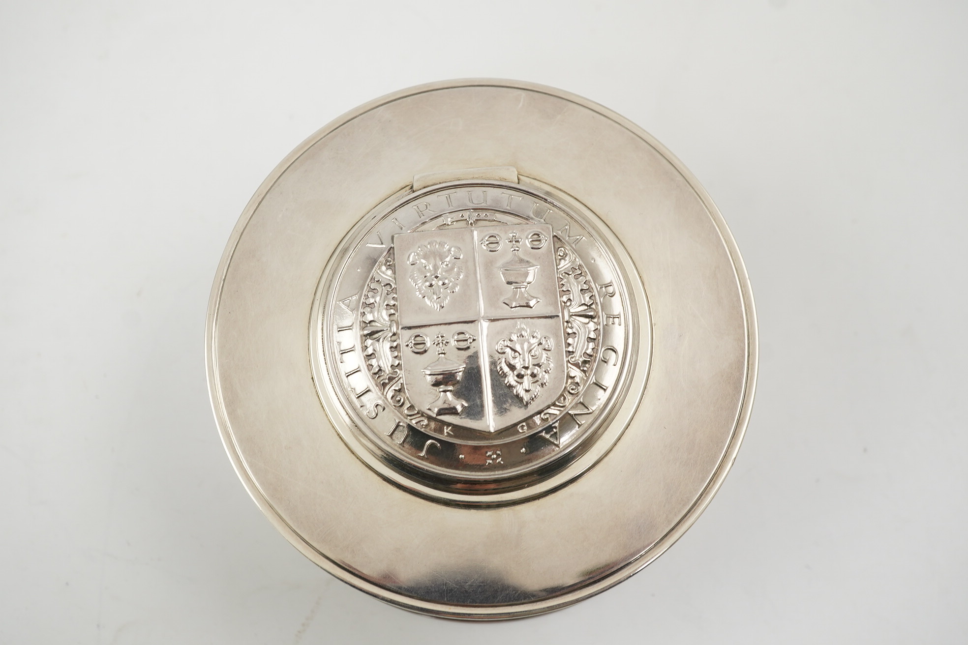 A George V silver circular inkwell, by Sebastian Garrard, commemorating the Silver Jubilee of King George V, the die stamped cover designed by George Kruger Gray featuring the Goldsmiths Company Coat of Arms